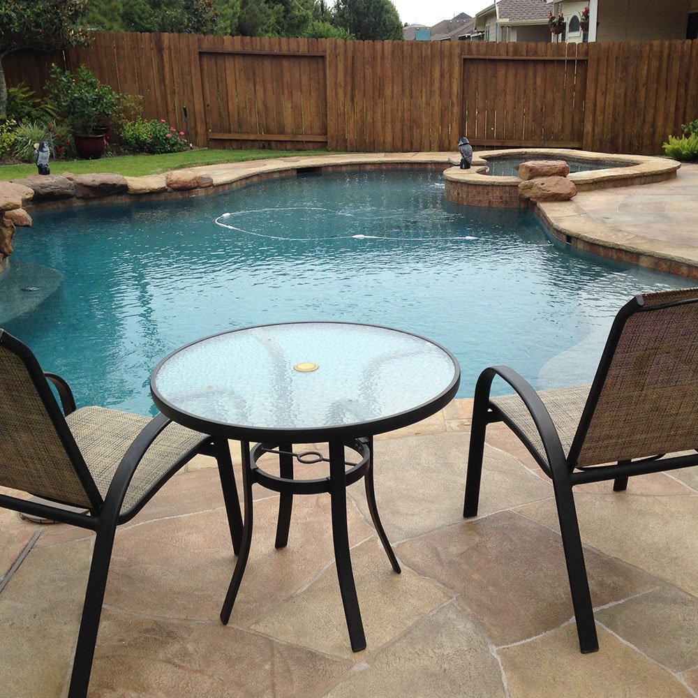 A serene poolside view featuring chairs and a table on a LimeCoat overlay deck, highlighting a smooth, stylish, and durable decking material offered by Houston Pool Renovations.